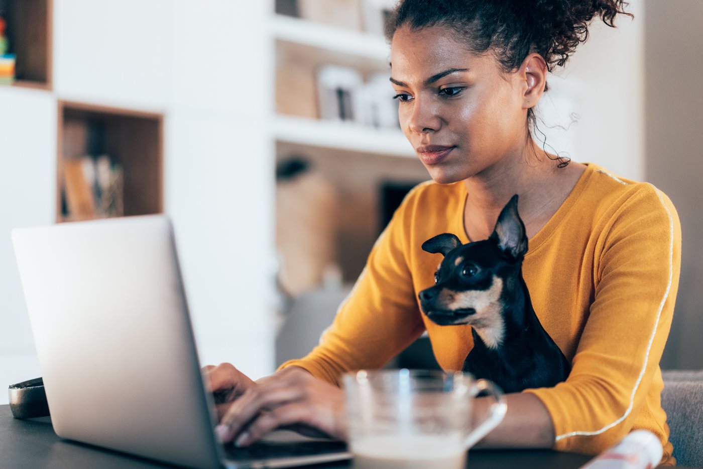 A young woman sits at her laptop with her dog in her lap while using Sparklight Internet