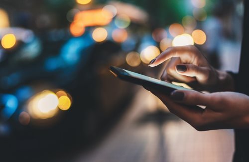 A woman's hand holds a mobile cellphone while waiting to cross the street