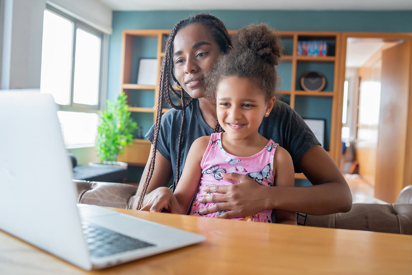 A young girl sits on her mom's lap while looking at a laptop